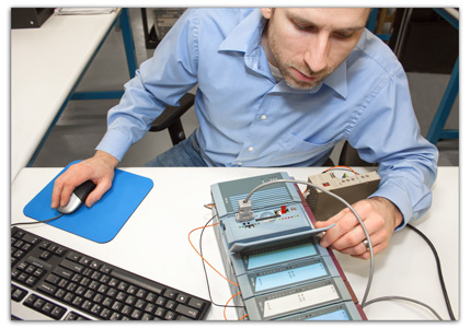 A person in a blue shirt uses a computer mouse, interacting with electronic equipment and tools on a workspace table