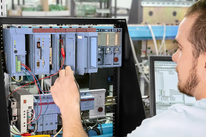 A technician manages wiring in a control panel packed with various electronic components and displays B&R 2005